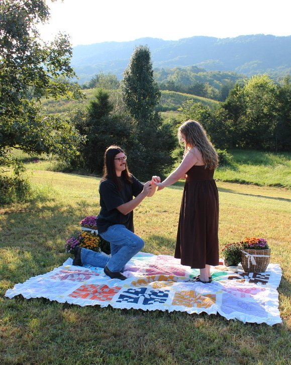 Parker and Jackson holding hands on a quilt in a mountain meadow, the day of the proposal